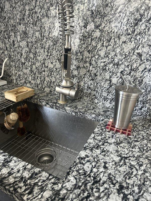 Responded to a broken kitchen faucet in a century-old residence where the issue had persisted for several days. Upon inspection, discovered a decorative chrome beverage tap with spiral coil design installed at a wet bar station with granite countertop. Examined under-sink plumbing and identified significant water damage and brown staining on cabinet interior walls, indicating active or previous leakage from supply lines or drain connections. Assessed P-trap assembly, supply line connections, and disposal unit for source of leak. Documented existing conditions including moisture damage and plumbing configuration for repair recommendations.