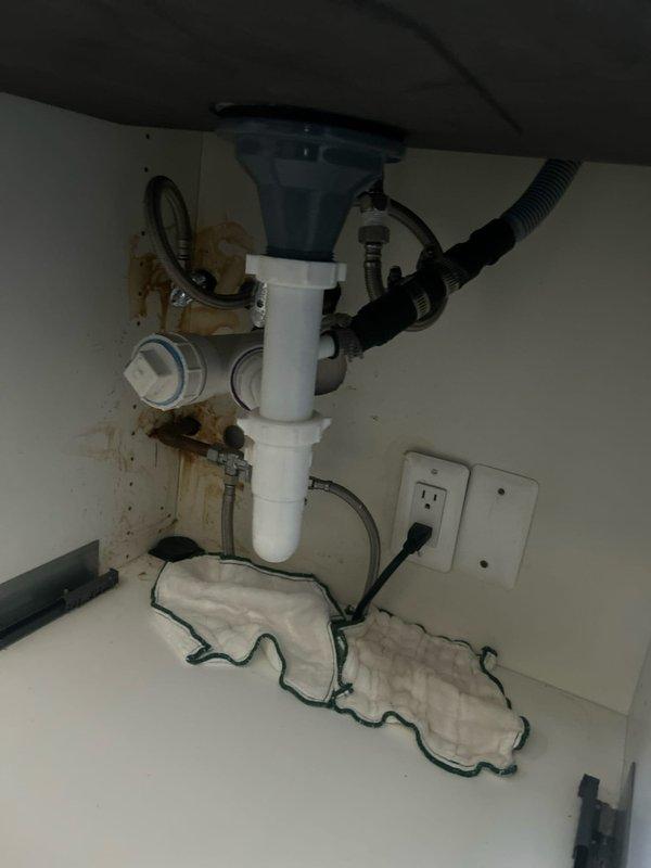 Responded to a broken kitchen faucet in a century-old residence where the issue had persisted for several days. Upon inspection, discovered a decorative chrome beverage tap with spiral coil design installed at a wet bar station with granite countertop. Examined under-sink plumbing and identified significant water damage and brown staining on cabinet interior walls, indicating active or previous leakage from supply lines or drain connections. Assessed P-trap assembly, supply line connections, and disposal unit for source of leak. Documented existing conditions including moisture damage and plumbing configuration for repair recommendations.
