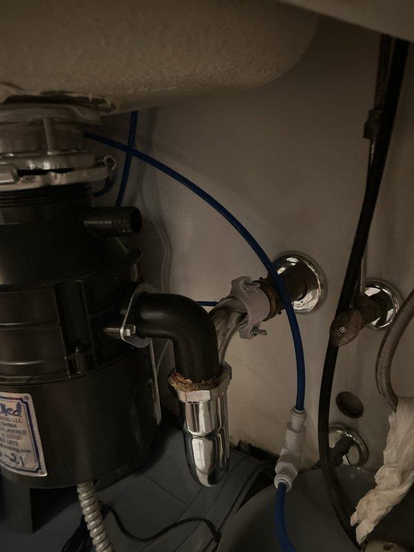Responded to kitchen sink leak in 17-year-old residence where water had been leaking for five days. Upon inspection, identified compromised connection at P-trap assembly beneath sink with garbage disposal unit. Disassembled chrome P-trap, inspected all drain connections including disposal discharge line and wall drain outlet, replaced worn washers and gaskets, and reassembled plumbing system ensuring proper seal at all connection points. Tested system thoroughly with water flow to verify leak resolution and proper drainage function.