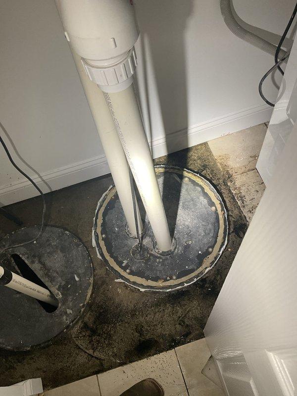 Responded to service call for water backup in basement near ejector pump and loss of cold water supply to shower. Upon arrival, inspected bathroom shower stall and identified plumbing issue affecting cold water delivery. Proceeded to basement utility area where extensive water staining and moisture damage was observed on concrete floor surrounding main plumbing stack penetration. 

Investigated ejector pump system and associated drainage lines. Found evidence of previous water backup events based on dark discoloration patterns radiating from pipe penetrations. Assessed white PVC piping configuration including main vertical stack and parallel drain lines. Examined threaded coupling connections and floor seal integrity around pipe penetrations. Noted corrugated discharge hose routing and pump components in utility space.

Cleared obstruction causing drainage backup and restored proper flow through system. Verified ejector pump operation and drainage functionality. Addressed cold water su