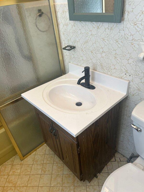 Completed professional installation of undermount oval sink with modern single-lever faucet onto newly constructed bathroom vanity cabinet with dark wood-grain finish. Installed all supply line connections, P-trap assembly, and verified proper drainage with no leaks detected. Conducted site assessment for future dishwasher installation in 1960s-era kitchen, evaluating existing plumbing infrastructure and determining requirements for water supply line relocation to accommodate new appliance placement in historic 1908 home.