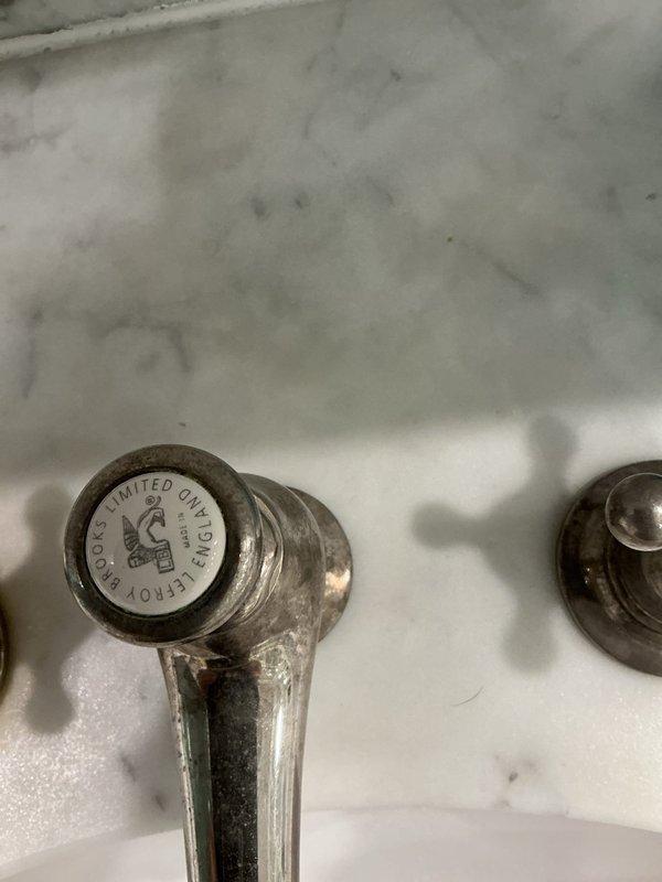 Responded to service call for leaking faucet handles in residential bathroom. Upon arrival, inspected double sink vanity configuration with traditional chrome faucets and separately examined vintage Chicago Faucet Co. fixtures showing significant age-related deterioration. Primary issue identified as leaking handles caused by worn internal components and deteriorated seals. Both affected faucet handles exhibited mineral buildup and corrosion consistent with extended service life. Assessed condition of fixtures, documented existing water damage and staining on surrounding porcelain surfaces, and provided recommendations for repair or replacement options to resolve the active leaks.