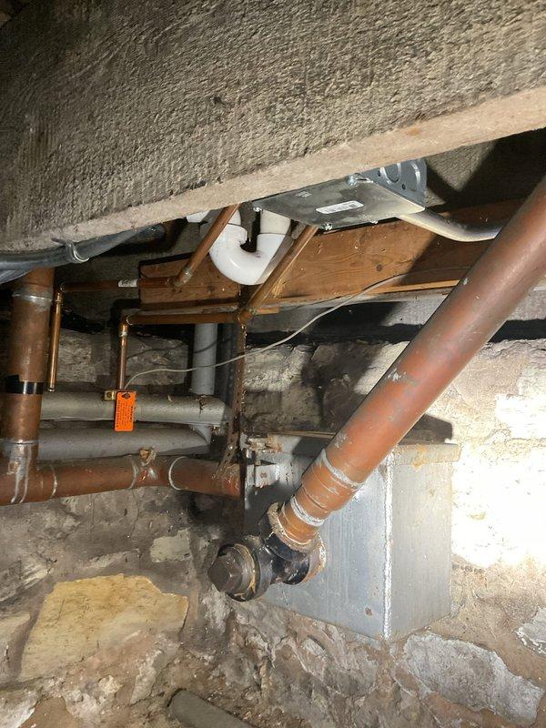 Responded to service call for slow draining kitchen sink and leak under sink. Upon inspection, identified drainage issue in kitchen sink P-trap assembly and confirmed active leak at pipe connections beneath sink cabinet. Inspected under-sink plumbing system including white PVC P-trap, supply lines, and shut-off valves. Examined basement/crawl space plumbing infrastructure including copper drain lines, PVC drainage piping, and associated fittings to assess overall drain line condition and identify potential blockage points. Documented existing plumbing configuration with photographs showing pipe routing, connections, and areas of concern for estimate preparation.