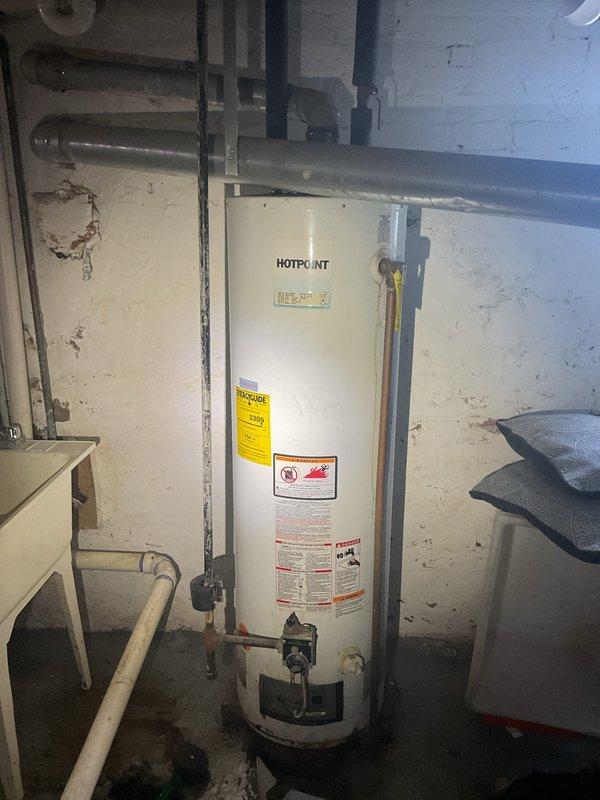 Conducted comprehensive assessment of residential water heating system following complete loss of hot water supply. Inspected existing Hotpoint water heater unit located in basement mechanical room and documented current installation configuration including all supply lines, drainage connections, and venting systems. Evaluated condition of copper supply piping, PVC drainage components, and existing shut-off valves. Photographed water heater unit showing manufacturer specifications, energy guide labels, and all plumbing connections to provide detailed documentation for replacement estimate. Assessed surrounding mechanical infrastructure including overhead floor joists, wall-mounted utilities, and available clearances for equipment replacement. Prepared comprehensive estimate for water heater replacement including all necessary materials and labor required to restore hot water service to the residence.