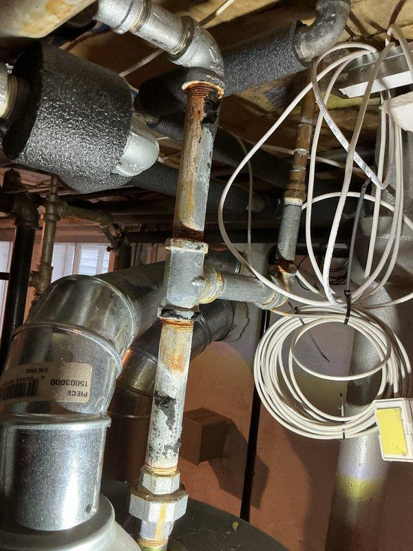 Responded to emergency call for active pipe leak at hot water heater in basement of century-old home. Upon inspection, identified corroded copper piping with failed threaded connections at water heater attachment point, showing significant rust and oxidation consistent with age and moisture exposure. Assessed entire plumbing network in utility area, noting extensive corrosion on multiple copper pipes, fittings, and galvanized metal components throughout the system. Shut off water supply to prevent further damage and leakage. Replaced compromised pipe section and corroded fittings connected to hot water heater using new copper piping and brass connections. Pressure tested all repairs to ensure leak-free operation and proper water flow. Inspected surrounding plumbing infrastructure for additional weak points requiring future attention due to advanced age of system. Restored water supply and verified hot water heater functionality with no active leaks present upon completion.