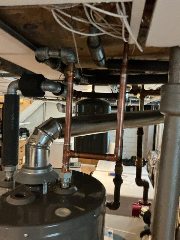 Responded to emergency call for active pipe leak at hot water heater in basement of century-old home. Upon inspection, identified corroded copper piping with failed threaded connections at water heater attachment point, showing significant rust and oxidation consistent with age and moisture exposure. Assessed entire plumbing network in utility area, noting extensive corrosion on multiple copper pipes, fittings, and galvanized metal components throughout the system. Shut off water supply to prevent further damage and leakage. Replaced compromised pipe section and corroded fittings connected to hot water heater using new copper piping and brass connections. Pressure tested all repairs to ensure leak-free operation and proper water flow. Inspected surrounding plumbing infrastructure for additional weak points requiring future attention due to advanced age of system. Restored water supply and verified hot water heater functionality with no active leaks present upon completion.