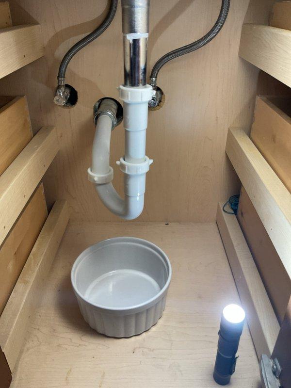 Responded to a clogged sink that had persisted for two weeks in a residential bathroom. Upon arrival, inspected the under-sink plumbing assembly, which consisted of white PVC P-trap configuration with chrome tailpiece extension and flexible supply lines. Assessed the drain system for blockages and proper venting. Cleared the obstruction using appropriate drain cleaning techniques, restoring full drainage capacity to the fixture. Tested water flow through the system to confirm proper operation and verified the P-trap seal was intact with no leaks present. All plumbing connections remained secure throughout the service, and the drain now operates at normal flow rate with no backup or slow drainage issues.