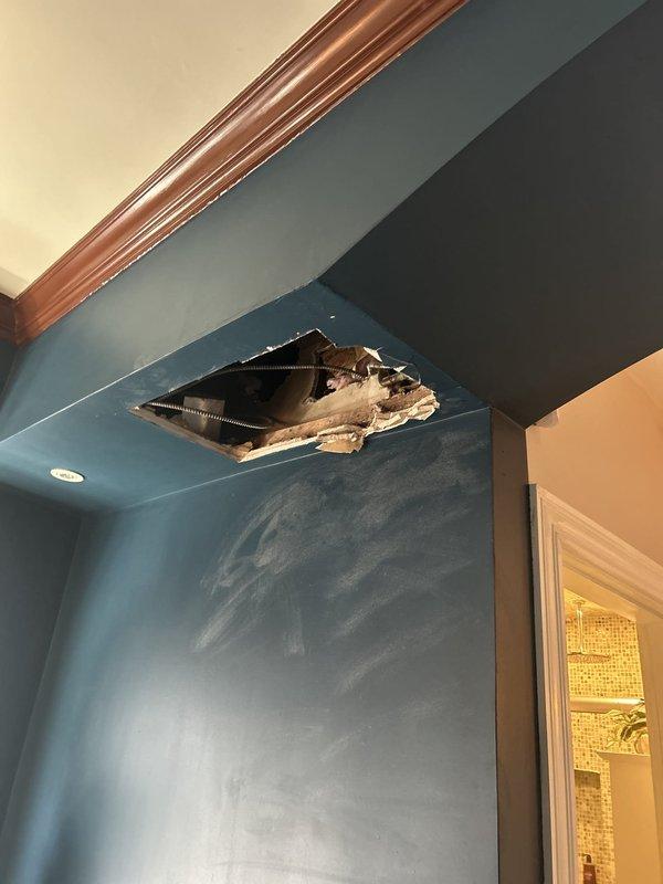 Accessed concealed plumbing system by creating opening in wall and ceiling above doorway to expose PVC drain line and HVAC ductwork. Removed drywall sections to provide necessary access for repair work, exposing wooden framing and mechanical systems behind finished surfaces. Awaiting deposit approval to proceed with complete repair and restoration of wall surfaces.