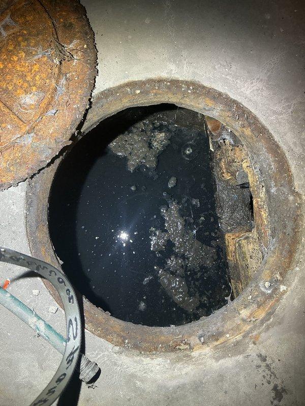 Completed residential drain and sewer assessment identifying need for new water valve replacement at building exterior and ejector pump installation with check valve in basement sump area. Documented existing conditions showing corroded access pit with standing water and deteriorated metal components, along with exterior plumbing infrastructure requiring valve upgrade. Provided estimate for necessary plumbing system improvements to address drainage and water control requirements.