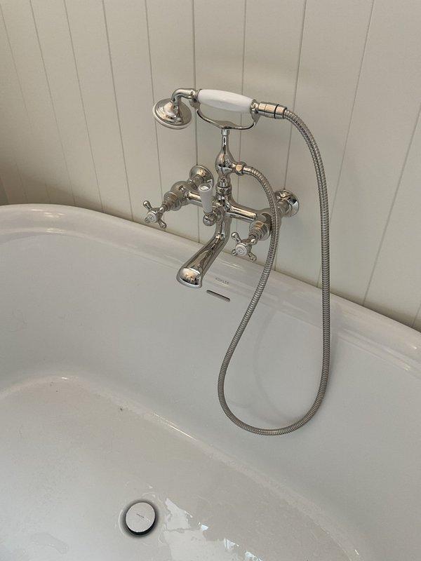 Responded to service call for low water pressure throughout the home following recent water heater installation. Conducted comprehensive inspection of plumbing system to identify cause of reduced flow. Examined freestanding bathtub fixture assembly with polished chrome and ceramic finishes, verifying proper operation of dual cross-handle controls and handheld shower component. Assessed water pressure at multiple fixtures to establish baseline measurements.

Inspected mechanical room installation including water heater connections and associated piping. Identified corroded horizontal pipe shaft and deteriorated components within floor-mounted circular access plate assembly. Evaluated white PVC discharge piping with visible wear and discoloration, along with adjacent pump or motor assembly showing signs of age. Checked all connection points for potential restrictions or blockages affecting system pressure.

Performed system diagnostics to determine if pressure issues stemmed from new wat