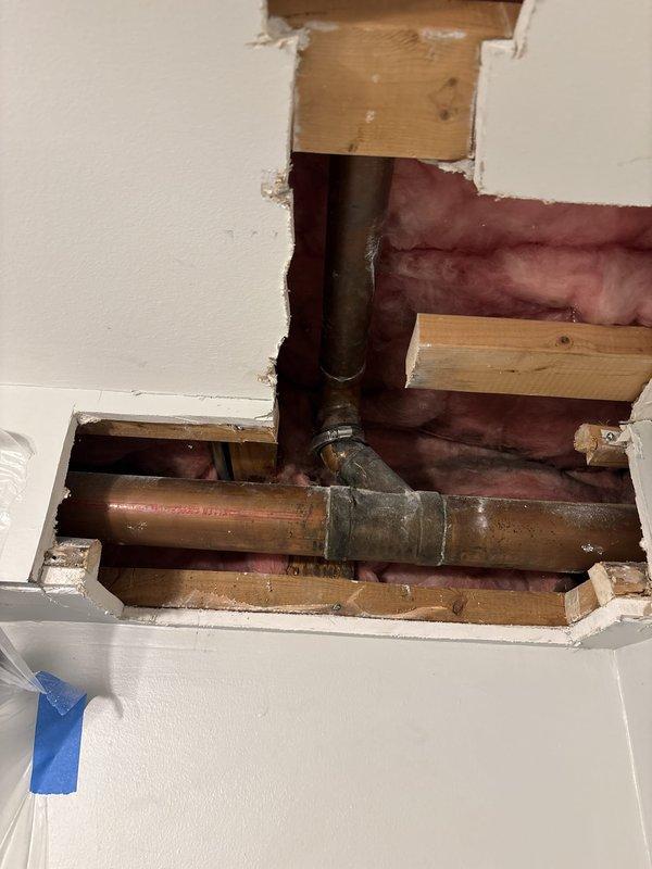 Accessed concealed plumbing system through wall opening in bedroom to address copper pipe concerns. Created drywall access point to expose vertical and horizontal copper supply lines with visible corrosion and patina buildup. Evaluated pipe condition, joint connections, and surrounding framing structure. Customer approved repair work, with partial payment received via check. Documentation photos captured of work area and exposed plumbing components.