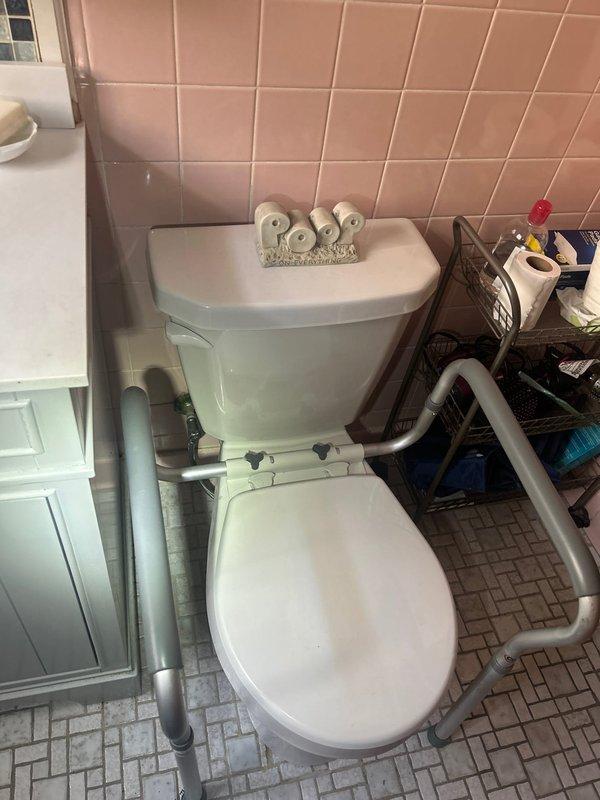 Completed toilet installation in residential bathroom with accessibility features. Verified 17-inch rough-in measurement and coordinated parts procurement prior to installation. Installed toilet fixture with surrounding grab bars for ADA compliance, ensuring proper positioning and secure mounting on existing tile flooring with herringbone pattern.