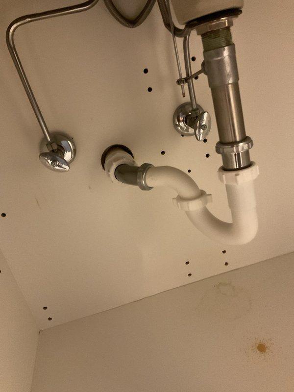 Responded to drainage issue in powder bathroom. Upon inspection, examined under-sink plumbing configuration including garbage disposal unit, P-trap assembly, and drain connections. Verified proper installation of chrome pop-up drain assembly with lift rod mechanism and confirmed white PVC drainage system connections. Inspected disposal mounting, water supply lines, and all pipe connections for leaks or blockages. Documented existing plumbing configuration showing disposal unit connected to drain system with appropriate trap configuration and venting.