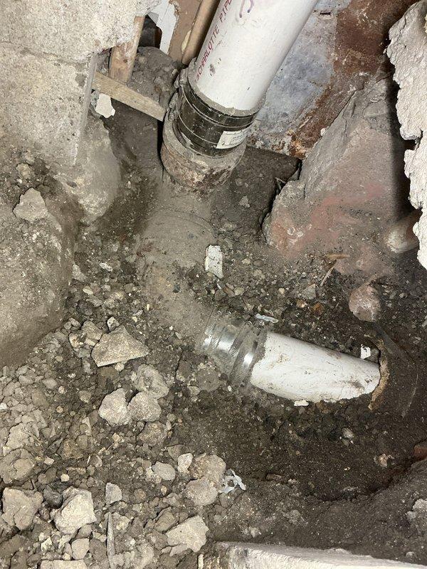 Responded to callback for toilet and sink reinstallation and discovered the root cause of recurring sewer backup issues. Upon investigation, identified that the existing 4" tee configuration had drain branches from the basement bathroom, laundry room, and toilet stack positioned lower than the main sewer line, creating an uphill flow condition that prevented proper drainage.

Broke up concrete flooring and excavated in storage room to expose the existing main sewer line. Removed the toilet stack from the no-hub coupling down to the horizontal connection point. Installed new toilet stack section using 4" PVC pipe and fittings, incorporating a new connection for ejector pump discharge, sump pump discharge tie-in, and cleanout access for future maintenance requirements. Connected the toilet stack to the main sewer using appropriate transition fittings to ensure code-compliant installation.

Installed new polyethylene ejector pit and ejector pump adjacent to the furnace location. Piped the