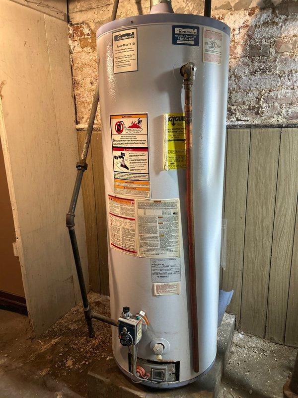 Conducted on-site assessment for water heater replacement in basement of 120-year-old residential property. Evaluated existing gas-fired water heater unit installed on concrete floor with copper supply lines, gas control valve assembly, and venting system. Documented current installation configuration including plumbing connections, gas line routing, temperature and pressure relief valve positioning, and exhaust venting through existing ductwork. Inspected surrounding utility area conditions including exposed stone foundation walls, clearance requirements, and access points for replacement work. Photographed existing unit specifications, manufacturer labels, energy guide information, and all visible piping connections to ensure proper sizing and specifications for replacement unit. Assessed gas supply line, cold water inlet, hot water outlet, and condensate drain configurations. Verified existing installation meets current code requirements for combustion air, venting, and safety clear