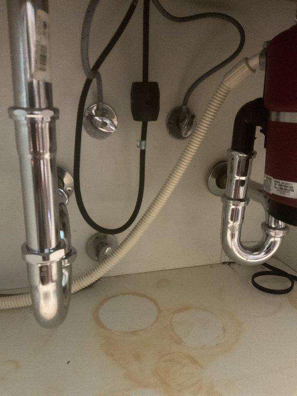 # Drain Replacement and Water Damage Assessment

Responded to service call for failed drain assembly under kitchen sink. Upon inspection, discovered significant water pooling and mineral staining on cabinet floor, indicating prolonged leak from deteriorated P-trap assembly. 

Removed and replaced corroded chrome P-trap connected to main sink drain and tailpiece assembly. Inspected adjacent plumbing components including garbage disposal connection, dishwasher drain line, and water filtration system to ensure no additional leak sources. All connections were tested for proper seal and drainage flow.

Cleaned and dried cabinet interior, removing standing water and residual contamination. Verified all drain connections are secure with no active leaks. System restored to full operational status.