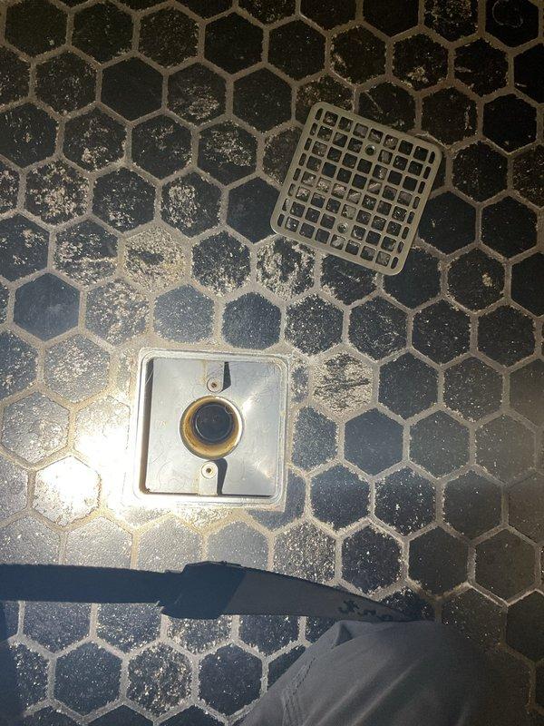 Responded to active bathroom leak in 20-year-old residence. Upon arrival, identified water accumulation on hexagonal tile flooring near floor drain assembly. Inspected drain cover, surrounding grout lines, and drainage components to determine source of moisture. Assessed ceiling and upper wall sections for potential leak origin points, checking for water damage or infiltration from above. Cleared debris from affected floor area, verified proper drain function, and confirmed leak source. Completed necessary repairs to stop active water intrusion and restore proper drainage operation.