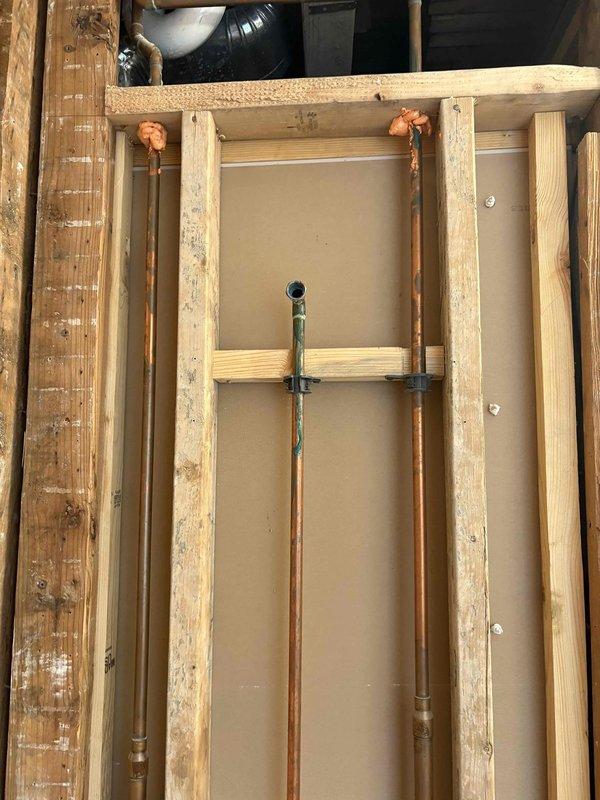 Conducted on-site assessment for shower valve replacement and plumbing stack evaluation. Inspected existing chrome-plated valve fixtures mounted on bathroom wall and examined exposed floor joists to evaluate copper supply line routing and condition. Documented deteriorated black pipe section at wall base, copper piping running through floor joists showing oxidation, and exposed subfloor structure with removed planking to facilitate access. Provided estimate for replacing shower valve with customer-supplied fixture and flange, as well as separate pricing for complete stack replacement based on observed pipe condition and accessibility through floor cavity.