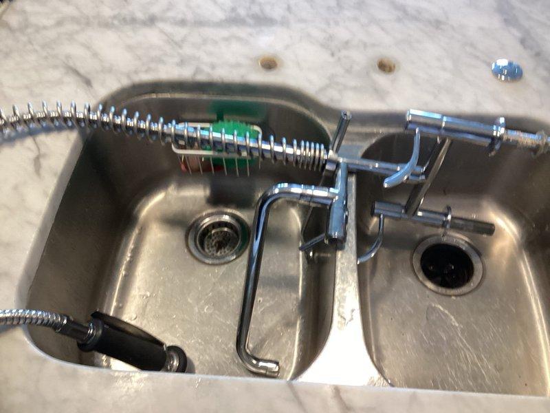 Completed installation of commercial-style pull-down kitchen faucet with pre-rinse spray head on double-basin stainless steel sink. Drilled mounting holes through marble countertop, secured faucet assembly with appropriate hardware, and connected water supply lines. Tested operation of pull-down spray mechanism and verified proper drainage in both sink basins upon completion.