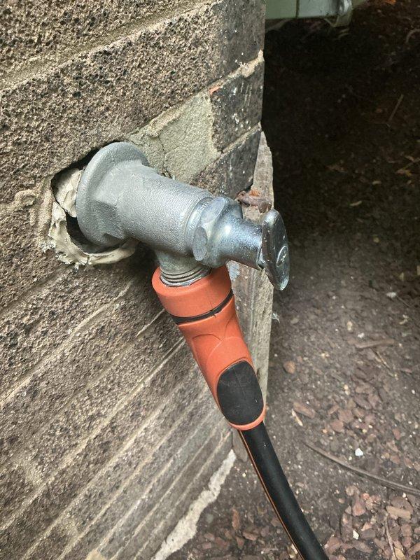 Completed main line drain and sewer installation with replacement of P-trap assembly and exterior hose bib connection. Installed chrome-plated P-trap with slip-joint fittings under wall-mounted fixture, ensuring proper trap configuration for drainage and sewer gas prevention. Replaced outdoor water spigot on concrete block wall with new galvanized valve body, applied sealant at wall penetration point, and connected rubber hose adapter to outlet for secure water distribution.