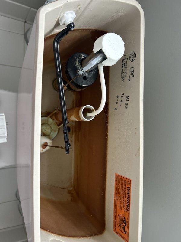 Responded to service call for toilet constantly running and not filling properly. Upon inspection, found severely deteriorated internal tank components with extensive rust contamination and sediment buildup in tank water. Fill valve assembly showed signs of malfunction with compromised float mechanism. Flush valve flapper exhibited wear and deterioration. Tank interior displayed significant rust staining and mineral deposits on porcelain surfaces and mechanical components, indicating long-term water quality issues and component degradation. Documented existing conditions with photographs showing brown-tinted water, corroded internal mechanisms, and compromised sealing surfaces. Assessed water supply line and shut-off valve functionality at floor connection. Provided estimate for complete tank rebuild including replacement of fill valve assembly, flush valve, flapper, and associated hardware to restore proper operation and eliminate continuous running condition.
