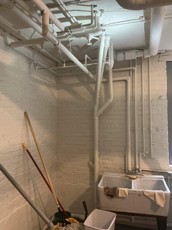 Completed kitchen stack repair involving extensive PVC drainage piping system in basement utility area. Repaired and reconfigured multiple sections of white PVC drain lines including horizontal ceiling runs and vertical drops, with proper mounting brackets and support hangers installed throughout. Work included addressing junctions, elbows, and connections serving the double-basin utility sink and associated plumbing fixtures to restore proper drainage function.