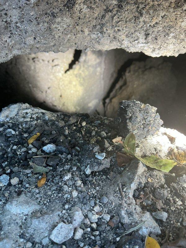 Responded to service request for sewer camera inspection due to sink hole in front of building. Performed comprehensive video camera inspection of main sewer line from house connection to street to assess condition and identify potential causes of ground subsidence. Documentation photos captured water meter assembly location and foundation area showing structural concerns with visible concrete deterioration, cracking, and debris accumulation beneath building structure.