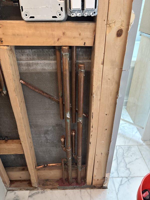 Capped off shower plumbing lines in bathroom undergoing renovation. Accessed exposed copper supply pipes within wall cavity and properly sealed termination points to prevent water flow to the shower fixture area. Work performed with wall framing exposed, allowing clear access to vertical copper piping system running through the stud cavity.