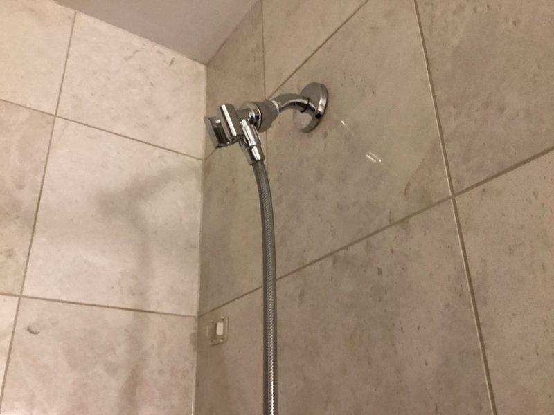 Responded to water leak at handheld shower diverter connection point. Upon inspection, found loose connection between diverter and shower arm with compromised seal causing active leak. Removed handheld showerhead assembly, applied thread seal tape to shower arm threads, and reinstalled diverter with proper torque to ensure watertight seal. Secured shower arm mounting bracket to wall to eliminate movement in trim assembly. Tested system under full water pressure to verify leak elimination and proper operation of handheld shower function.