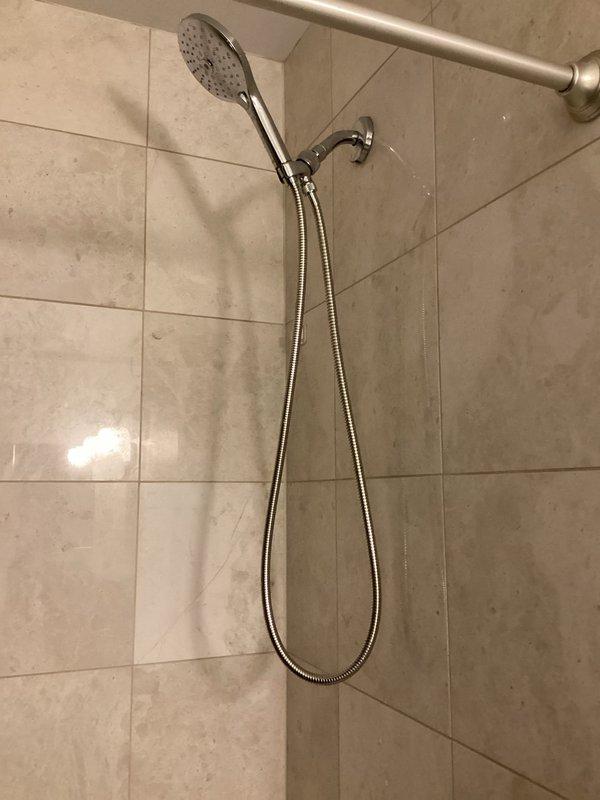 Responded to water leak at handheld shower diverter connection point. Upon inspection, found loose connection between diverter and shower arm with compromised seal causing active leak. Removed handheld showerhead assembly, applied thread seal tape to shower arm threads, and reinstalled diverter with proper torque to ensure watertight seal. Secured shower arm mounting bracket to wall to eliminate movement in trim assembly. Tested system under full water pressure to verify leak elimination and proper operation of handheld shower function.