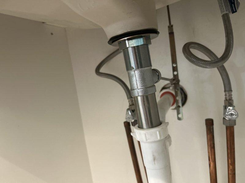 Installed three-piece chrome faucet assembly with lever-style handles and center spout on gray marble countertop with undermount white basin. Connected braided stainless steel supply lines to existing copper supply pipes and installed pop-up drain assembly with stopper mechanism. Return visit required to address improper installation of faucet handles and drain pull mechanism that did not meet quality standards.