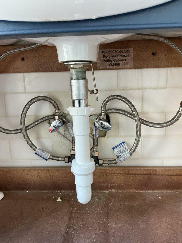 Responded to ongoing hot water temperature fluctuation issue following previous tankless water heater installations. After determining tankless systems were not resolving the intermittent hot water delivery problem, converted system to tanked water heater configuration. Installed new tank-type water heater with associated components including expansion tank, pressure relief valve, and supply connections. Replaced existing plumbing connections under kitchen sink with new braided stainless steel supply lines and chrome shutoff valves with color-coded indicators. Updated drain assembly with white PVC components and vacuum breaker fitting. System tested and verified for consistent hot water delivery without temperature fluctuations.