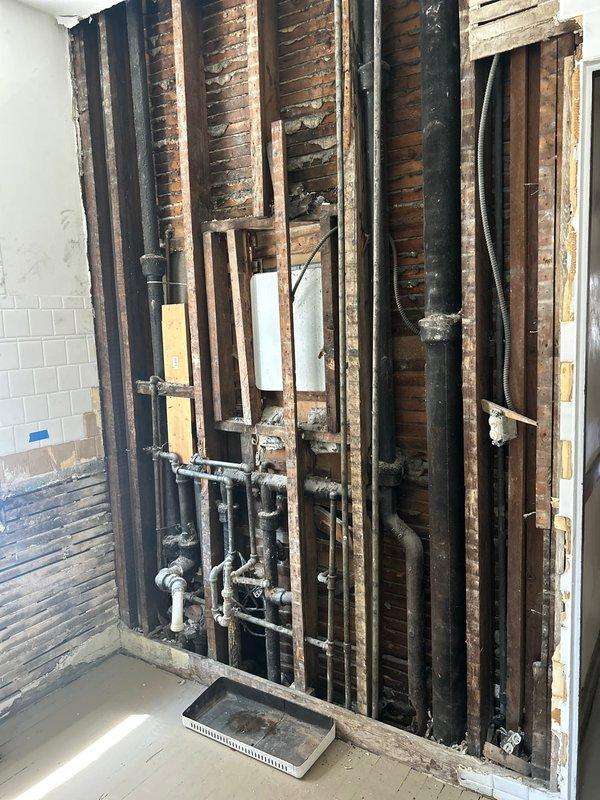 Completed comprehensive plumbing piping installation in bathroom renovation area, involving installation of mixed PVC and metal supply and drainage lines within exposed wall cavity and floor joist system. Integrated new plumbing infrastructure with existing cast iron drainage components, including proper fitting connections, elbows, and joints to ensure code-compliant water distribution and waste removal systems throughout the renovated space.