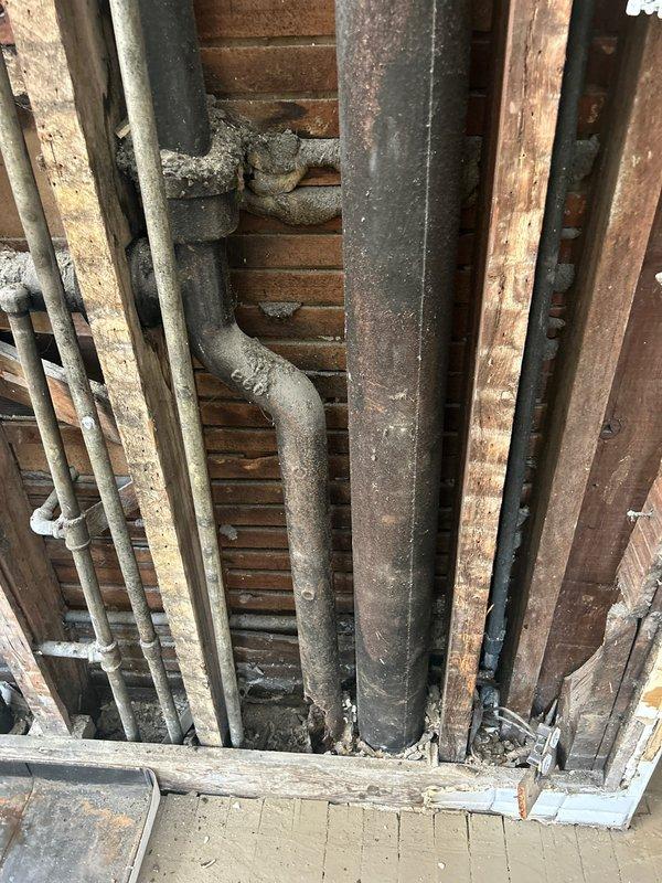 Completed comprehensive plumbing piping installation in bathroom renovation area, involving installation of mixed PVC and metal supply and drainage lines within exposed wall cavity and floor joist system. Integrated new plumbing infrastructure with existing cast iron drainage components, including proper fitting connections, elbows, and joints to ensure code-compliant water distribution and waste removal systems throughout the renovated space.
