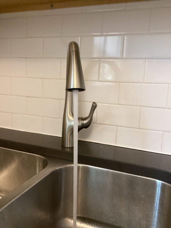 Responded to low water pressure complaint affecting kitchen and bathroom sinks in unit 2 of century-old residential property. Upon inspection, assessed existing plumbing infrastructure including undermount stainless steel kitchen sink with modern brushed stainless steel faucet and associated supply lines. Examined under-sink plumbing configuration revealing PVC drainage system with metallic braided flexible supply lines connected to faucet assembly. Evaluated water flow at both affected fixtures to determine pressure loss patterns and potential causes related to aging galvanized piping common in older homes, mineral buildup in aerators or supply lines, or partially closed shut-off valves. Documented existing conditions through photographic evidence showing current fixture installation, countertop mounting, and under-sink plumbing arrangement including supply hoses, drain connections, and shut-off valve accessibility. Investigated potential restriction points in water delivery system an