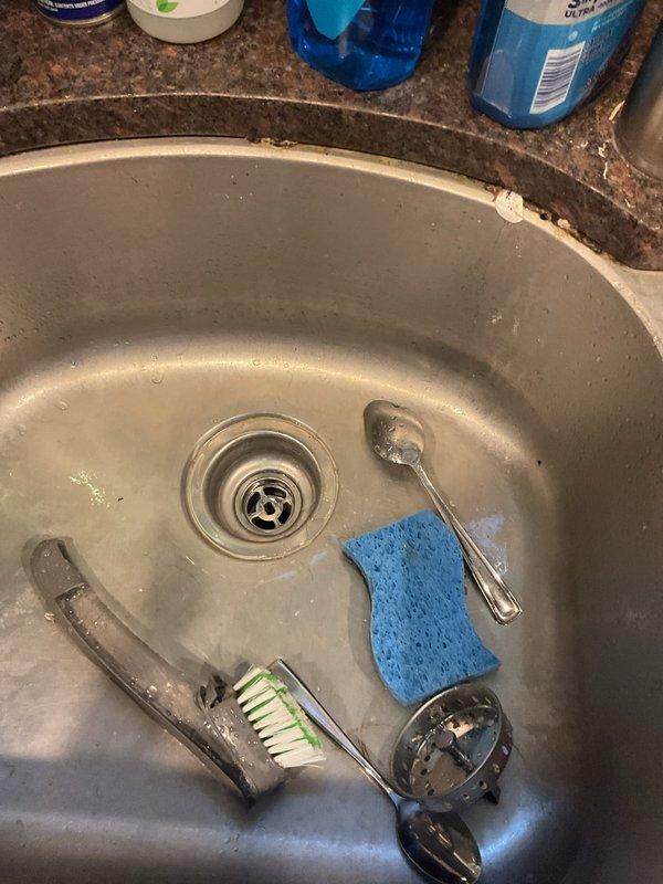 Inspected kitchen sink drain assembly and P-trap plumbing connections beneath basin. Documented existing drain basket strainer, white PVC P-trap assembly with slip-joint fittings, and associated drainage piping showing mineral deposits and age-related discoloration. Verified proper trap configuration for sewer gas prevention and assessed overall condition of under-sink plumbing components.