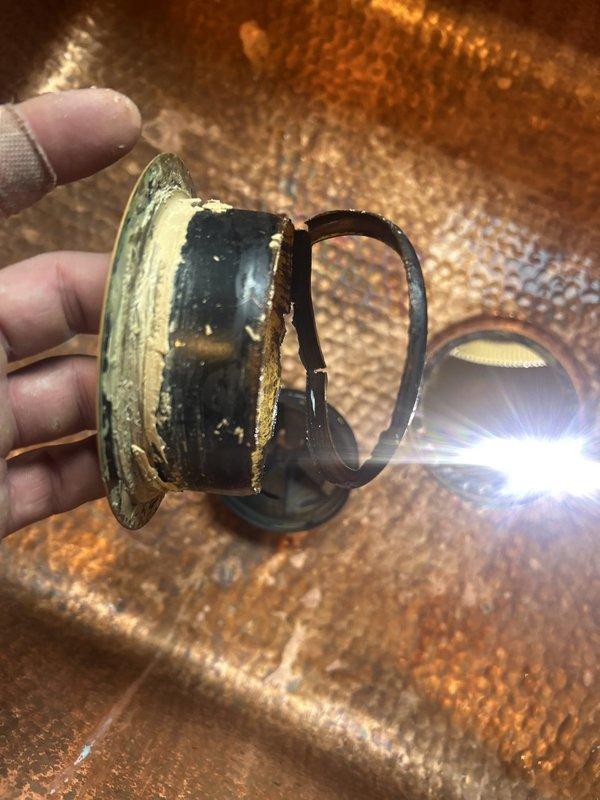 Responded to water leak between kitchen sink and garbage disposal. Upon inspection, located failed garbage disposal mounting flange assembly showing severe corrosion and structural deterioration. The mounting flange exhibited extensive pitting, material breakdown, and complete cracking of the gasket seal, which was the source of the active leak. Documented the damaged components and existing plumbing configuration under the sink, including disposal unit connections and drainage system. Advised on necessary repairs to eliminate the leak and prevent further water damage to the cabinet area.