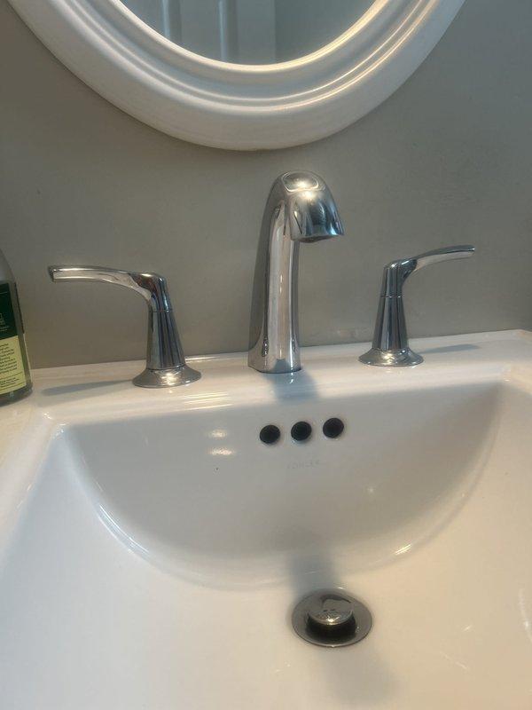 Installed new three-piece chrome faucet assembly on white pedestal sink, including central arched spout and dual lever handles for hot and cold water control. Verified proper water flow, tested drain pop-up assembly operation, and confirmed no leaks at all connection points.