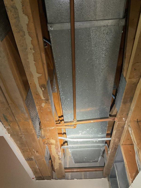 Responded to water leak investigation with wall already opened and exposed for access. Inspected walk-in shower stall showing visible streaking and discoloration on shower pan surface, examined exposed ceiling/floor joist cavity with HVAC ductwork to locate leak source. Documented conditions with photos of shower enclosure and opened wall cavity for further assessment and repair recommendations.