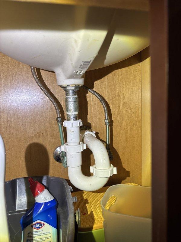 Completed installation of under-sink plumbing assembly including white PVC P-trap configuration with proper drain connections and flexible braided metal supply lines for hot and cold water. All components installed to code with secure fittings and proper trap seal for drainage system functionality.