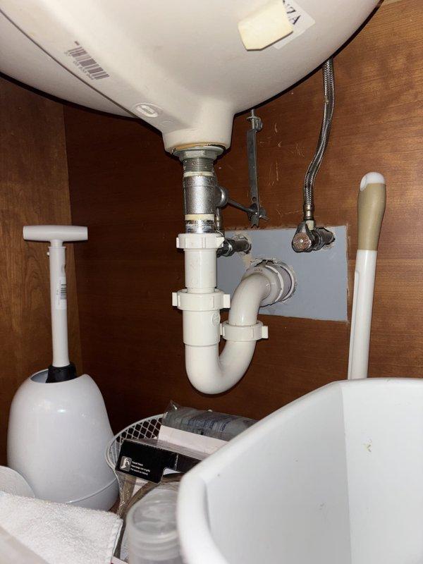 Completed installation of under-sink plumbing assembly including white PVC P-trap configuration with proper drain connections and flexible braided metal supply lines for hot and cold water. All components installed to code with secure fittings and proper trap seal for drainage system functionality.
