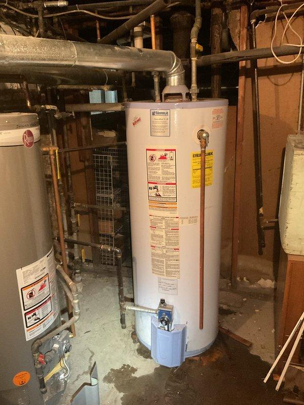 Conducted commercial drain and sewer estimate inspection of basement utility area housing multiple water heating systems. Documented existing plumbing infrastructure including extensive copper piping network, PVC ductwork, and water heater installations with thermostat controls and safety specifications. Assessment revealed aging mechanical components with visible dust accumulation on thermostat housing and connections, requiring evaluation for potential drain line servicing and preventative maintenance recommendations.