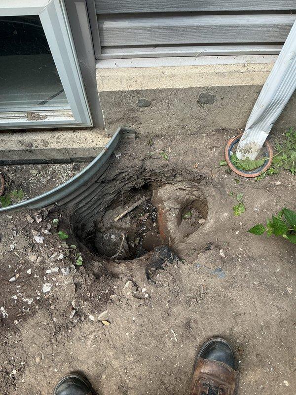 Completed sewer line installation at residential property where existing infrastructure showed severe deterioration with heavily rusted piping at the foundation connection point. Excavated access area adjacent to building foundation, removed compromised section of corroded sewer pipe, and installed new black corrugated drainage line with proper slope and connection to existing system. Documented pre-existing conditions showing extensive rust damage to original piping and backfilled excavation upon completion of installation.