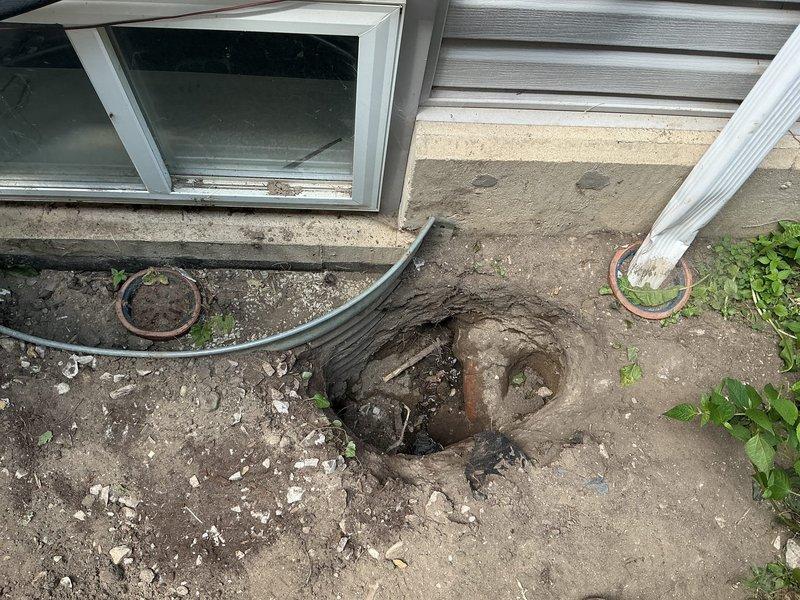 Completed sewer line installation at residential property where existing infrastructure showed severe deterioration with heavily rusted piping at the foundation connection point. Excavated access area adjacent to building foundation, removed compromised section of corroded sewer pipe, and installed new black corrugated drainage line with proper slope and connection to existing system. Documented pre-existing conditions showing extensive rust damage to original piping and backfilled excavation upon completion of installation.
