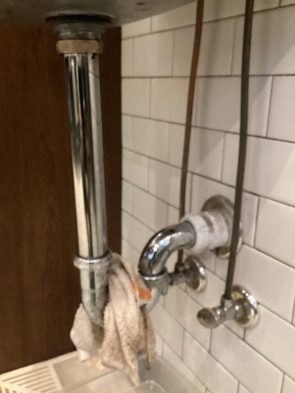 Responded to commercial plumbing service call for hand washing sink with cracked pipe. Upon inspection, identified deteriorated chrome P-trap assembly showing significant corrosion, water staining, and compromised structural integrity. Documented existing plumbing configuration including copper supply lines, chrome shutoff valves, and drain connections mounted against subway tile wall. Photographed damaged trap assembly and surrounding plumbing components to provide visual documentation of condition requiring repair or replacement.