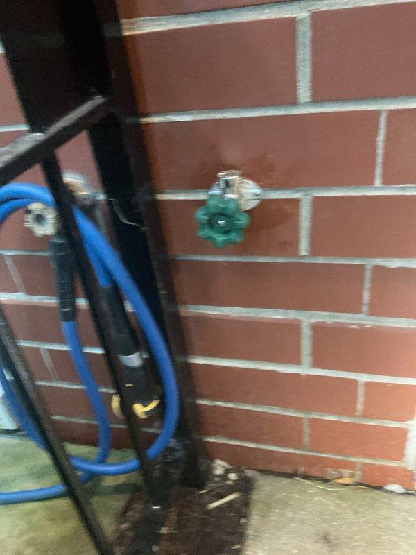 Installed new plumbing fixture with copper pipe connections behind drywall access point. Cut access panel in interior wall to route and connect copper supply lines using brass fittings and shutoff valve, with exterior green valve mounted on brick wall for main water control.