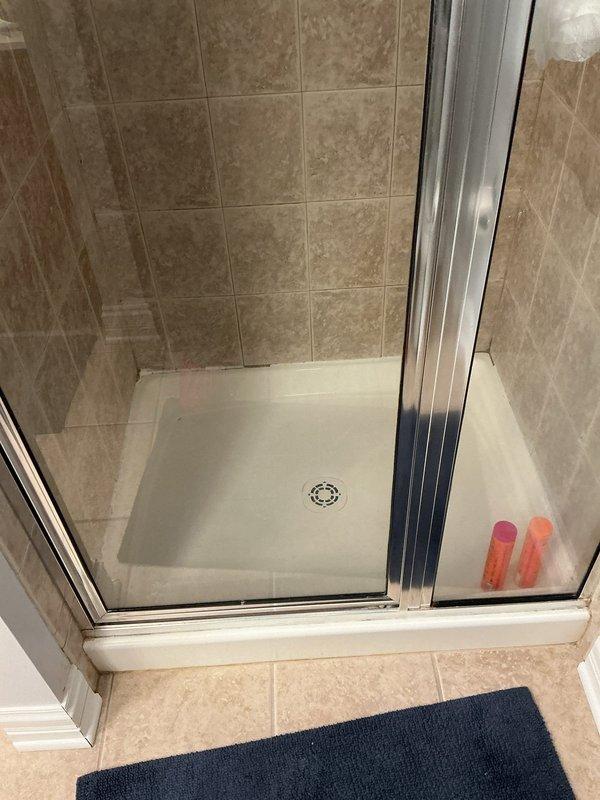 Responded to reassess water leak with ceiling already opened for access. Upon inspection of the bathroom shower area, examined the shower enclosure, tiled walls, glass door assembly, and surrounding fixtures for signs of moisture intrusion or active leaking. Documented conditions with photographs showing the beige marble-effect tiled shower walls, white shower pan with center drain, chrome-framed glass door assembly, and bathroom floor area. No active water leakage was observed at the time of inspection, and all visible plumbing fixtures, shower components, and tile surfaces appeared to be in good condition with proper drainage function.