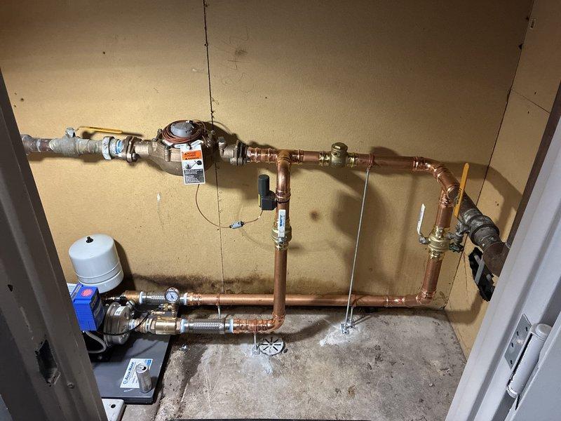 Completed installation of a comprehensive water treatment system including a recirculation pump with expansion tank, backflow preventer, and multi-valve copper piping configuration with shut-off controls at key points. The system was mounted in the utility room with proper pressure regulation components and flexible connections to ensure optimal water quality and circulation throughout the property. All components were tested and verified operational upon completion.