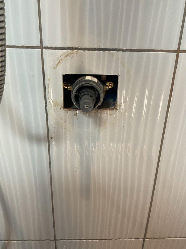 Completed plumbing repair service involving a recessed wall-mounted fixture in a tiled bathroom environment. Addressed water damage and staining around the installation area, with component secured and operational. Documentation photographs captured for service records.
