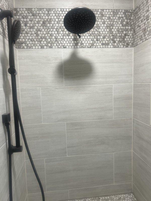 Responded to low water pressure complaint in modern walk-in shower equipped with dual shower system including ceiling-mounted rainfall showerhead and wall-mounted handheld unit with slide bar, all featuring matte black thermostatic valve controls. Upon inspection, identified issues with shower valve distribution and water supply lines affecting flow to both the overhead rainfall fixture and handheld shower components. Documented existing installation showing large-format tile work with decorative penny-round mosaic accents and professional plumbing fixture placement. Diagnosed distribution valve requiring repair to restore proper water pressure throughout the dual shower system. Captured detailed photographic documentation of shower configuration, fixture positioning, and tile work for reference. Scheduled follow-up appointment to provide repair estimates for shower valve and distribution water line corrections necessary to resolve pressure issues and restore full functionality to both